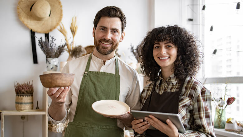 Two small business owners. A man holds a finished product, a woman a tablet.