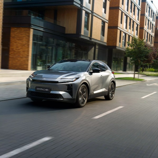 Pilkas modernus elektrinis visureigis „Toyota“ važiuoja vingiuotu keliu, apsuptu žalumos ir medžių.